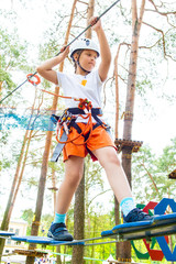 Young girl in harness climbing and trying facilities in an adventure park.