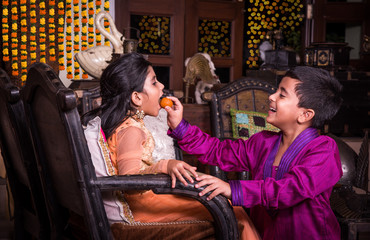 indian siblings eating laddu on diwali or festival, kids celebrating diwali festival with sweets