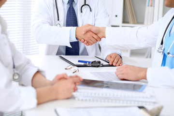 Two doctors shaking hands to each other sitting at the table in hospital office