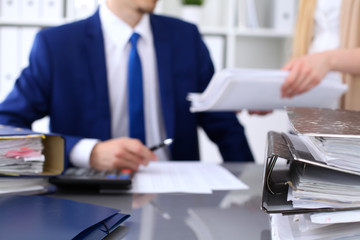 Binders with papers are waiting to be processed with businessman and secretary back in blur....