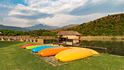 Mullti-colored canoes next to the dam at Champagne Castle, in the Drakensberg. Cathkin Peak in the...