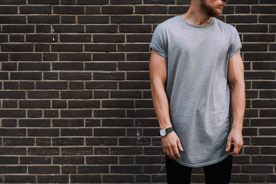 A cropped photo of a bearded muscular hipster guy wearing a blank gray t-shirt with the  empty space for the logo or design. Mock up.