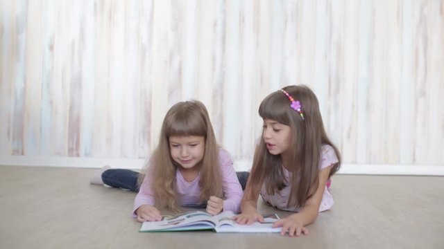two little girls reading a book lying on the floor