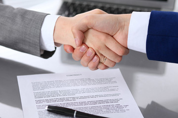 Businessman and business woman shaking hands to each other above signed contract