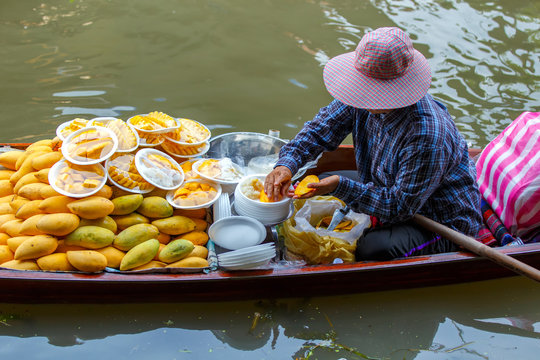Asian woman peeling the mangoes are for sale thai dessert "Mango sticky rice" at Damnoen Saduak floating market in Ratchaburi near Bangkok, Thailand