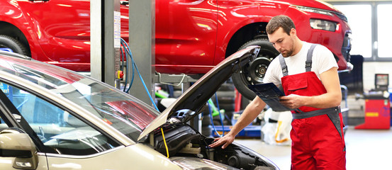 Kundendienst in einer Autowerkstatt - Mechaniker kontrolliert Fahrzeug - obrazy, fototapety, plakaty