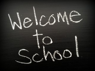 The phrase Welcome to School written in white chalk on a blackboard A vignette has been added for effect