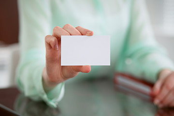 Business woman hands in a green blouse sitting at a desk in an office and holds out business card.
