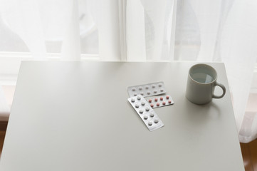 white pills lying next to a glass of water on a wooden table