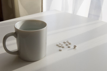 Fototapeta na wymiar white pills lying next to a glass of water on a wooden table