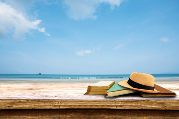 hat and book on wood terrace over tropical island beach background.