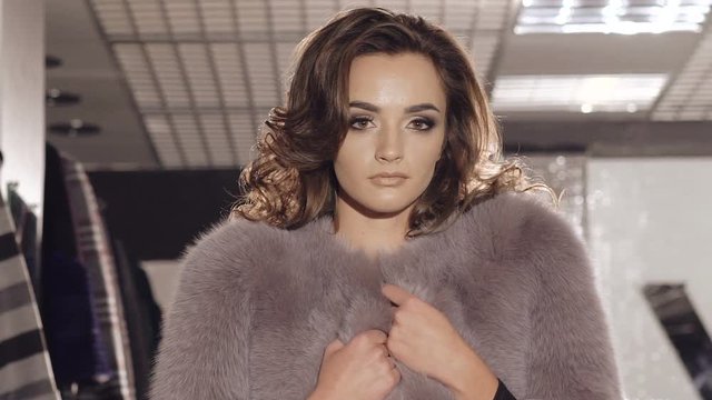 Enjoyable model posing in rich fur coat in boutique for camera
