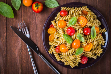 Fusilli pasta salad with pesto genovese, colorful tomatoes and basil leaves on dark wooden background top view. Italian cuisine. Delicious meal.