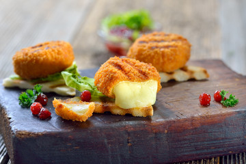 Toast mit heißen Mini-Camemberts und Preiselbeeren -Toasted panini triangles with breaded mini camembert cheese loaves, cranberries and iceberg lettuce served on a wooden cutting board - obrazy, fototapety, plakaty