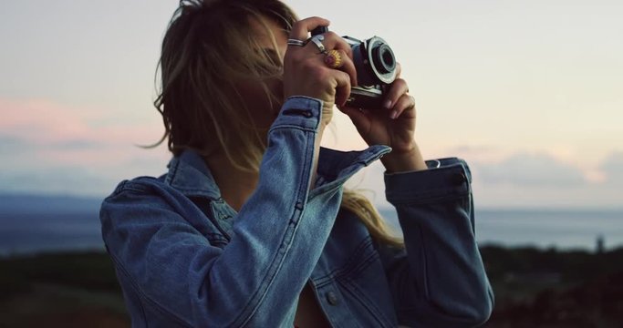 Beautiful young woman with vintage camera taking pictures at sunset, fashion lifestyle