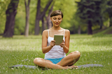 Young woman using tablet outdoor siting on grass, smiling.