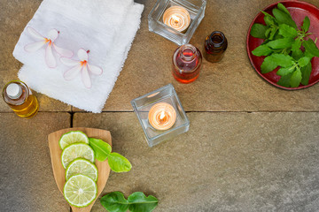 Aromatic oil, burned candle, pink flowers, sliced  lime, green leaf, white towel on vintage grunge stone background, spa treatment concept