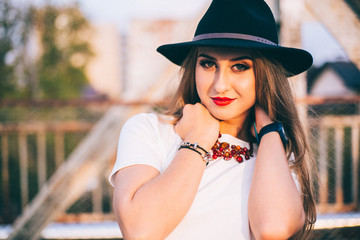 Outdoor lifestyle close up portrait of happy blonde young woman in stylish casual red dress (skirt) and black hat  stay on bridge on the street. Pretty hipster girl having fun and enjoying holidays.