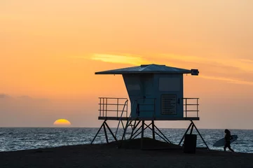 Fotobehang Silhouette of Surfer running past lifeguard tower during sunset on Huntington beach in southern California © Gabriel Cassan
