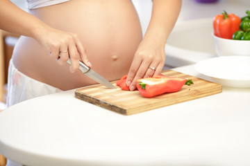 Obraz na płótnie Canvas pregnant woman cuts the pepper in the kitchen, close up