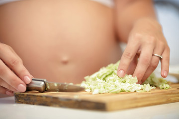 pregnant woman cuts cabbage on wooden Board, close-up