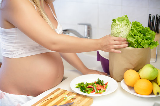 pregnant woman at kitchen preparing salad, close up
