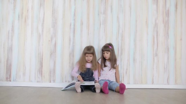 two little girls reading a book sitting on floor