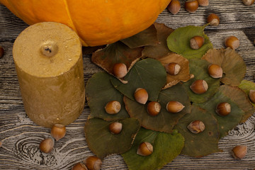 yellow pumpkin, leaves, candle, hazelnut on wooden background