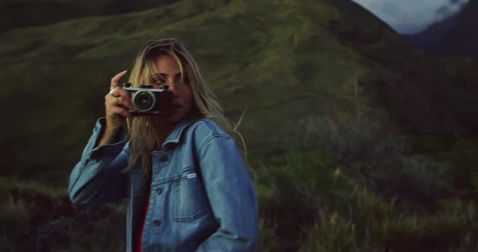 Beautiful young woman with vintage camera taking pictures at sunset, fashion lifestyle