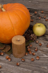 yellow pumpkin, leaves, candle, cone, apple, hazelnut on wooden background