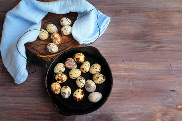 Quail eggs on a wooden table with cast iron pan and blue napkin. Toned image, special light. Top view, copy space.