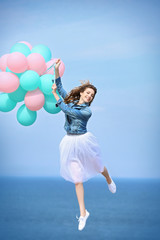 Beautiful young woman with colorful balloons on sea front