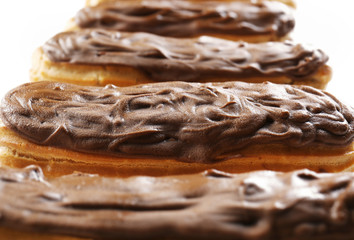 Delicious chocolate eclairs in row on white background, closeup