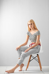 Pretty young woman in casual clothes sitting on chair against light background