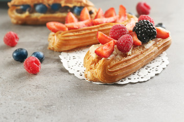 Delicious eclairs with berries and doily on light textured background
