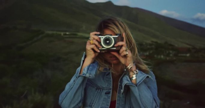 Beautiful young woman with vintage camera taking pictures at sunset, fashion lifestyle