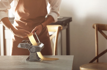 Man using pasta machine to prepare dough for tagliatelle, close up view