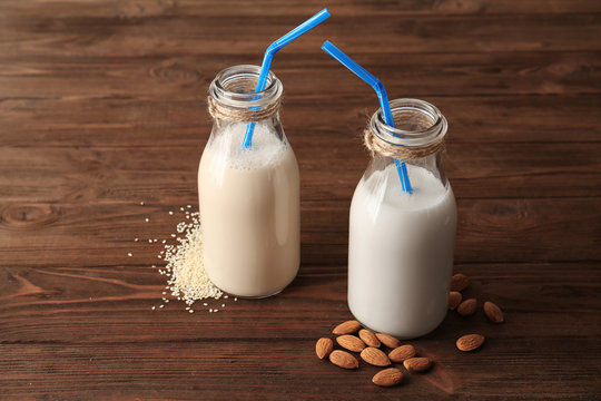 Bottles of sesame and almond milk with straws on wooden table