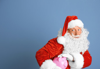 Santa Claus holding piggy bank on blue background