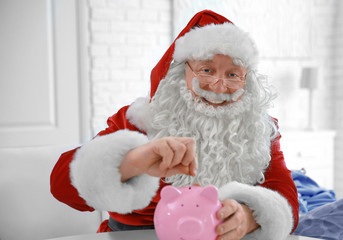 Santa Claus putting coin into piggy bank at home