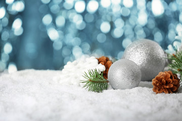 Christmas baubles, cone and coniferous branch on snow against defocused lights