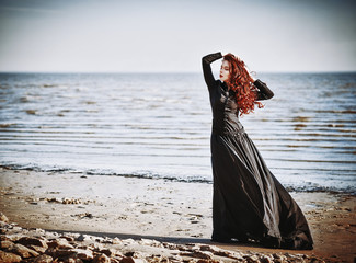 Beautiful sad goth girl standing on sea beach