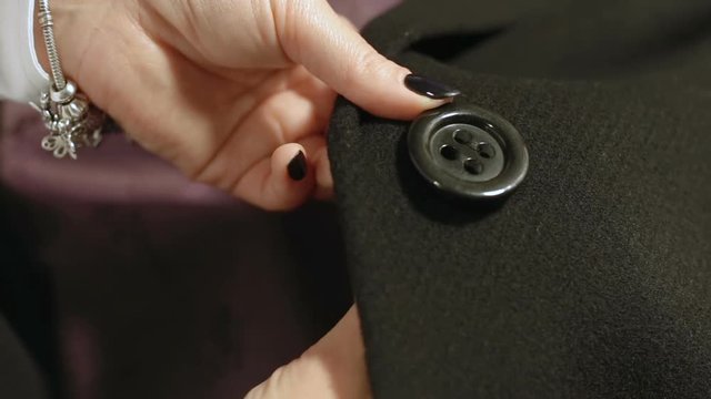 Woman sews a button to black black coat.