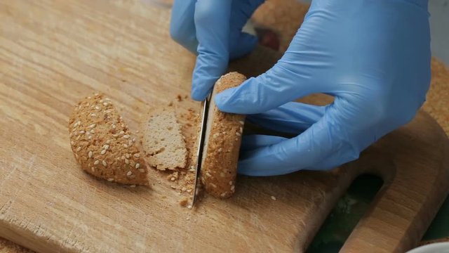 Woman in blue gloves cut into pieces of oatmeal cookies with sesame seeds to test the quality.