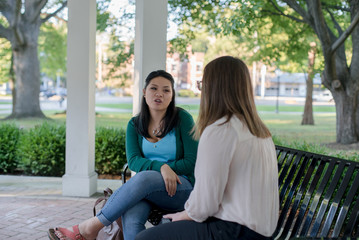 College aged female friends sitting and talking under a gazebo in a park