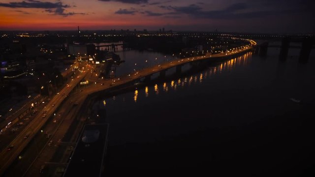 Aerial View of European City at Night with Illuminated Light from Cars, Bridge Over the River. Shot in 4K UHD