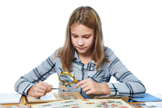 Teen girl with magnifier looks his stamp collection isolated