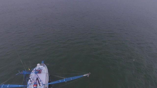 Aerial flyover of a shrimp boat trawling in open water in the Atlantic ocean, dragging its nets while seagulls fly around.