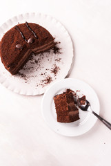 Chocolate cake with cream on a white wooden table. One piece of cake is on the plate, top view, copy space