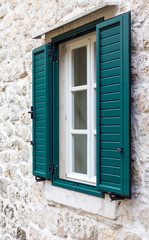 Fototapeta na wymiar a window in the wall of stone with open green shutters
